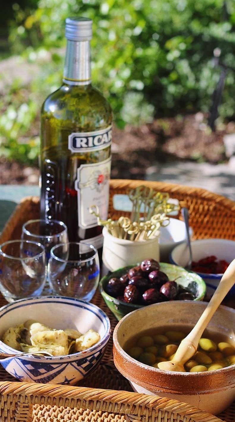 Pastis, olives and aperitif on a wicker tray in a Provençal garden